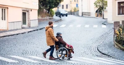 Una persona joven paseando a una persona mayor en silla de ruedas