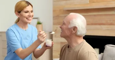 una cuidadora dando un yogurt a un anciano