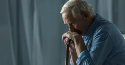 Persona mayor sentada en el sofa con la barbilla encima de su bastón