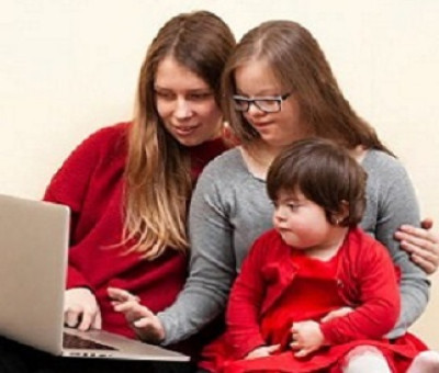 Una persona enseñando a manejar un ordenador a otras dos con discapacidad cognitiva (una adolescente y un bebé)