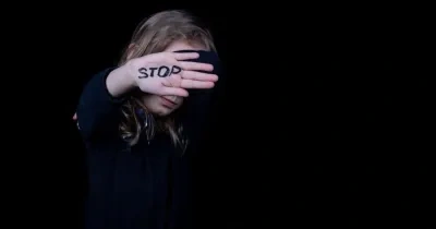 Una mujer pide el fin de la violencia de género con la palabra "stop" pintada en la mano mientras se tapa la cara con ella