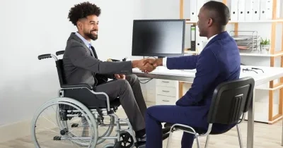 Dos trabajadores, uno de ellos en silla de ruedas y otro sin discapacidad visible, chocando sus manos en forma de acuerdo alcanzado en un despacho de la oficina