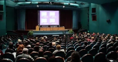 foto de un auditorio de una universidad con alumnos ocupando sus localidades y una mesa rectangular en el escenario