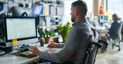 vista lateral de un hombre ocn silla de ruedas trabajando en un ordenador