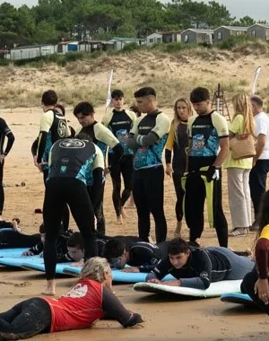 Participantes y monitores de una actividad de surf adaptado reciben formación en la playa de Loredo durante el I Festival de Parasurf Fundación También–Plea. Varias personas practican la posición sobre tablas de surf en la arena mientras un grupo observa y se prepara para entrar al agua. La imagen muestra una jornada de deporte inclusivo y aprendizaje junto al mar Cantábrico.