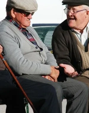 Tres mayores conversan sentados en un banco 