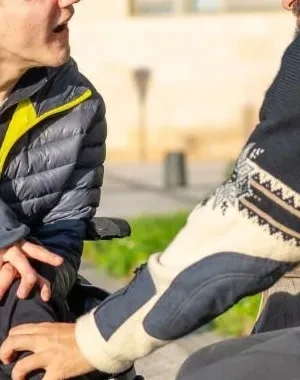 Dos hombres, un de ellos en silla de ruedas y el otro sentado en un banco, hablando