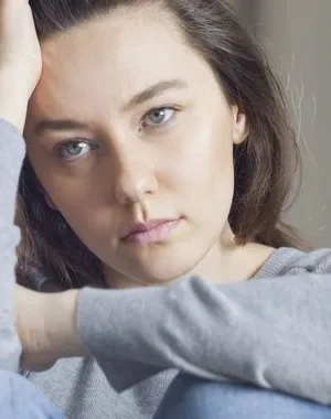 Una mujer sentada en el sofá de rodillas tocándose el pelo