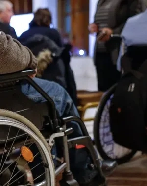 Dos personas con silla de ruedas caminando por u palacio muy regio en el que les reciben ciertas personas