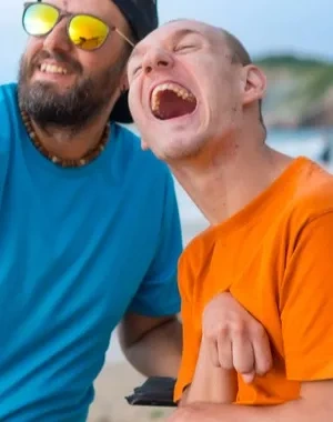 Una persona sin discapacidad junto a una persona con discapacidad en silla de ruedas haciéndose un selfie en la playa