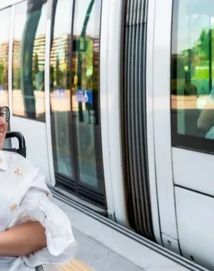 Un hombre sin discapacidad junto a una mujer en silla de ruedas esperando en el andén al tren