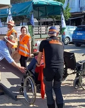 Varias personas voluntarias subiendo a una usuaria en silla de ruedas a un autobús turístico.