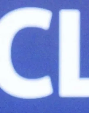 Alt text:  Persona interviniendo desde un atril durante la jornada de presentación de “Finanzas Inclusivas”. La imagen muestra a la persona junto a dos micrófonos mientras realiza una exposición ante el público. Al fondo aparece una gran pantalla azul con el texto “Jornada de Presentación de Finanzas Inclusivas” y los logotipos de las entidades organizadoras. El acto forma parte de la presentación de la renovación del recurso formativo impulsado por Fundación ONCE para promover la educación financiera inclu