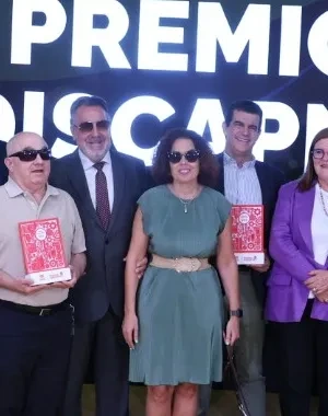 Foto de grupo de las personas premiadas, representantes institucionales y asistentes durante la VIII edición de los Premios Discapnet de Fundación ONCE. Los participantes posan sobre un escenario frente a una gran pantalla con el texto “Premios Discapnet VIII” y los logotipos de Fundación ONCE y Grupo Social ONCE. Varias personas sostienen los galardones, mientras que en la primera fila también aparecen una persona usuaria de silla de ruedas eléctrica y un perro guía tumbado en el suelo