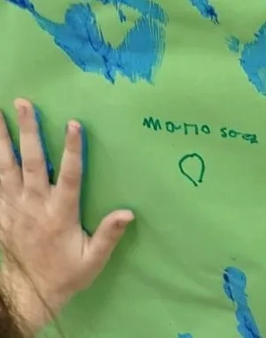 nila con manos llenas de pintura dejando su huella en un papel en la pared