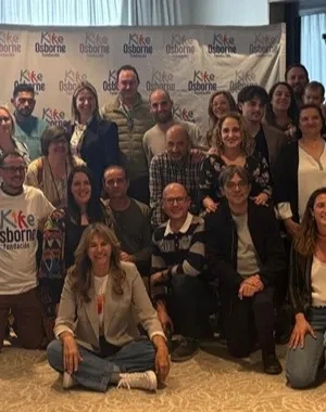 Foto de grupo de familias, profesionales y personas con discapacidad reunidas en una sala, posando juntas tras el taller “Adolescencia, familia y discapacidad” de la Fundación Kike Osborne en Valencia, con un photocall de la Fundación al fondo.