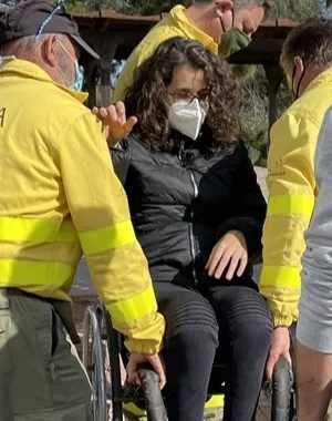 Tres técnicos de emergencias levantando a pulso a una usuaria en silla de ruedas, haciendo un ejemplo práctico con un supervisor que explica