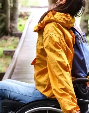 Una mujer en silla de ruedas posando en un camino de madera rodeado de árboles