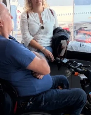 Persona con silla de ruedas esperando a embarcar en un avión, que puede verse al fondo por una cristalera