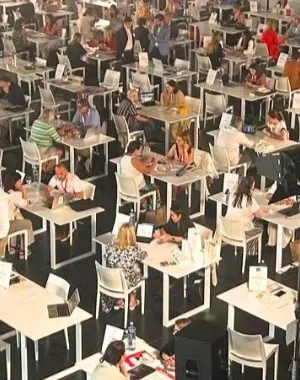 Salón de juntas con varias mesas y muchos ponentes y oyentes