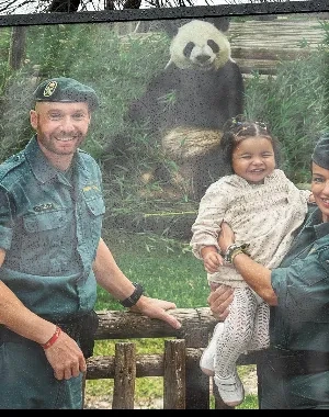 Dos miembros de la Guardia Civil posan junto a una niña delante del recinto de un panda gigante en un parque zoológico. Las tres personas se encuentran junto a una valla de madera, mientras el animal aparece al fondo rodeado de vegetación. La imagen forma parte de una acción de sensibilización vinculada al calendario solidario de la Guardia Civil.
