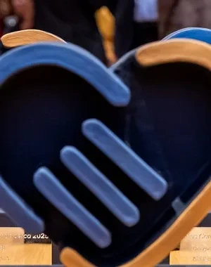 Los 5 premios que se entregarán en la gala delante y, al fondo, personas organizadoras