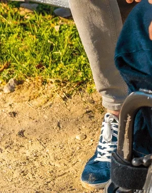 Persona en silla de ruedas y otra persona mantienen una conversación en un parque urbano con zonas verdes y caminos peatonales.