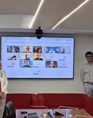 Participantes del grupo de la reunión con una pantalla digital en la que estaban proyectando una sesión virtual con otros participantes