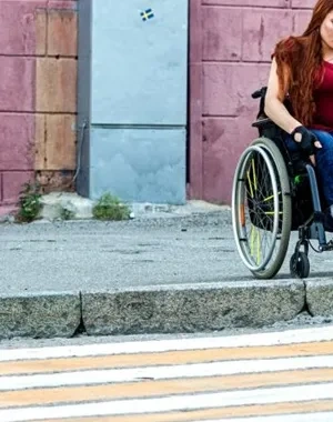 Una chica joven en silla de ruedas dispuesta a pasar por un paso de peatones, pero no puede debido al bordillo que impide seguir su camino