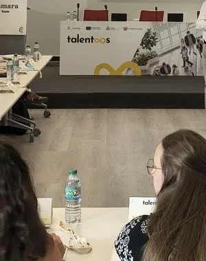 Muchas personas sentadas en una mesa con una ponente en el medio que modera y dirige la sesión