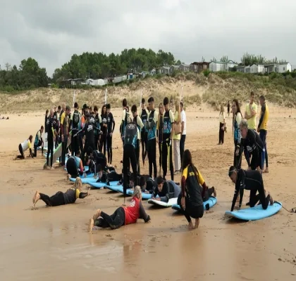 Participantes y monitores de una actividad de surf adaptado reciben formación en la playa de Loredo durante el I Festival de Parasurf Fundación También–Plea. Varias personas practican la posición sobre tablas de surf en la arena mientras un grupo observa y se prepara para entrar al agua. La imagen muestra una jornada de deporte inclusivo y aprendizaje junto al mar Cantábrico.