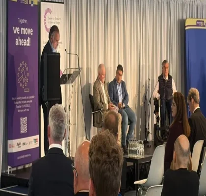 Los ponentes subidos en el escenario del evento, con un moderador en el atril y a su espalda el cartel de AccesibleEU