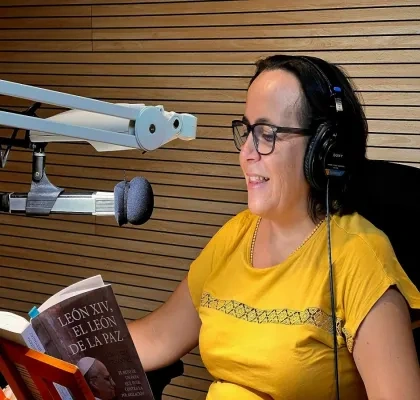 Persona con auriculares sentada en un estudio de grabación frente a un micrófono profesional mientras lee el libro León XIV, el León de la paz, de Almudena Hernández. La imagen muestra la grabación de la versión sonora de la obra, con paneles acústicos de madera al fondo y el ejemplar abierto sobre un atril.