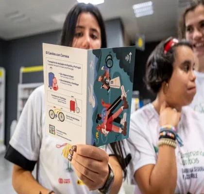 Participantes en una actividad del proyecto Camino + Accesible sostienen un folleto informativo de El Camino con Correos, que recoge servicios para peregrinos como el transporte de equipajes, el envío de bicicletas y la consigna en Santiago de Compostela.