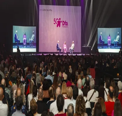 Dos personas subidas en el escenario hablando sentados en dos sillas, mientras hay multitud de personas en la grada observando 