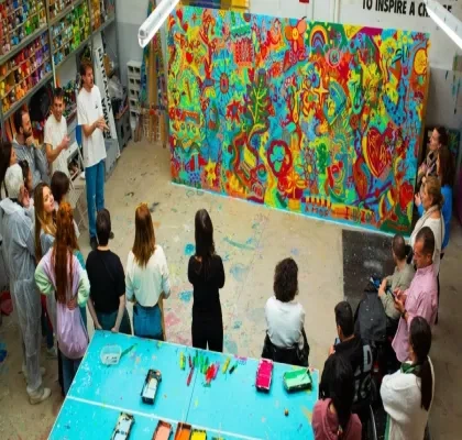 Foto Creación Ilusión con varias personas presenciando la obra, que es un mural grande con mucho colorido.