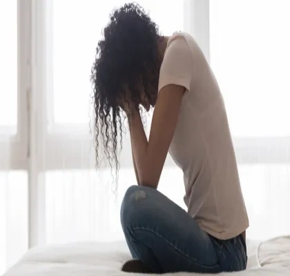 Mujer en la cama sentada con los brazos en la cara mostrando soledad o tristeza