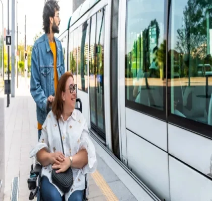 Un hombre sin discapacidad junto a una mujer en silla de ruedas esperando en el andén al tren