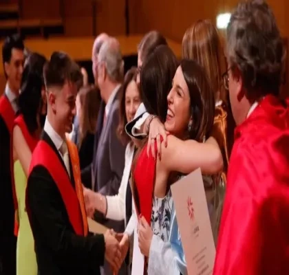 Una foto de dos alumnos recibiendo el título de los profesores de la universidad y dándose un abrazo