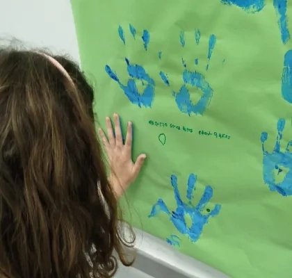 nila con manos llenas de pintura dejando su huella en un papel en la pared