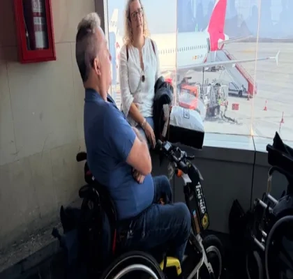 Persona con silla de ruedas esperando a embarcar en un avión, que puede verse al fondo por una cristalera