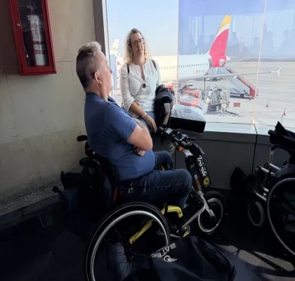 hombre en silla de reudas observando un avión desde una ventana