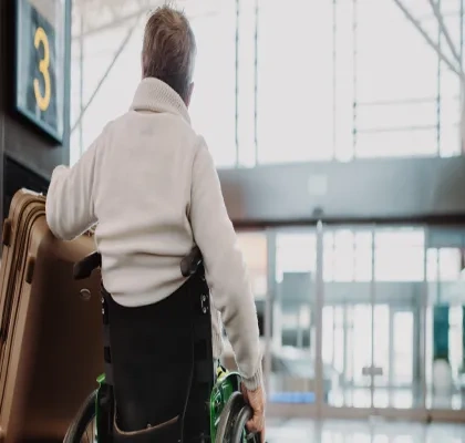 Un hombre con silla de ruedas, al que se ve de espaldas, movíendose por el aeropuerto con su maleta