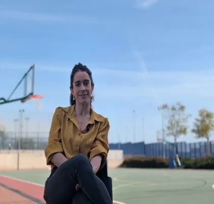Una de las impulsoras del estudio, posando a cámara sentada en una pista de atletismo y baloncesto de fondo.