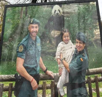 Dos miembros de la Guardia Civil posan junto a una niña delante del recinto de un panda gigante en un parque zoológico. Las tres personas se encuentran junto a una valla de madera, mientras el animal aparece al fondo rodeado de vegetación. La imagen forma parte de una acción de sensibilización vinculada al calendario solidario de la Guardia Civil.