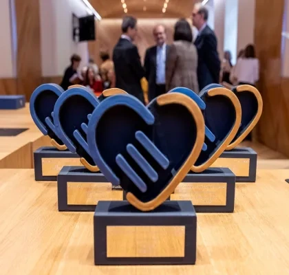 Los 5 premios que se entregarán en la gala delante y, al fondo, personas organizadoras