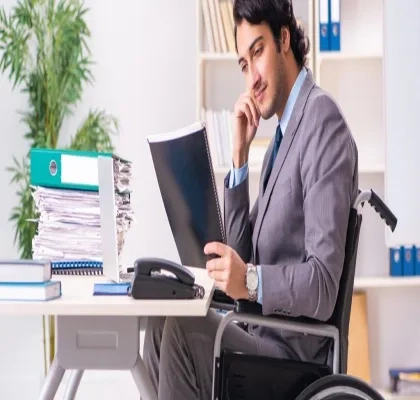Persona con discapacidad física que va en silla de ruedas traajando en el escritorio con su ordenador y cuadernos.