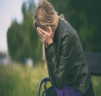 Mujer jóven sentada en un banco se tapa la cara con las manos