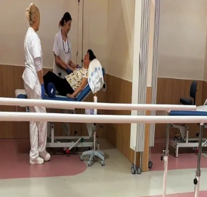 En un box de un hospital, una doctora y una enfermera hablan con una paciente encamada