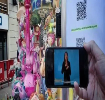una falla de fondo mientras se está apuntando con un movil al código QR y está describiendo en la pantalla una mujer la falla valenciana